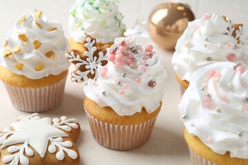 Tasty cupcakes with Christmas decor and gingerbread cookies on white table, closeup