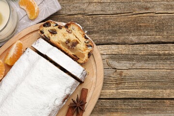 Traditional Christmas Stollen with icing sugar, spices, tangerine and candle on wooden table, flat lay. Space for text