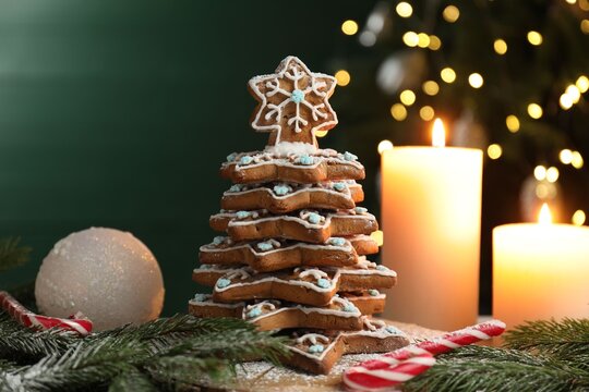 Christmas tree made of gingerbread cookies, fir branches, candy cane and burning candles against green background with blurred lights - Powered by Adobe