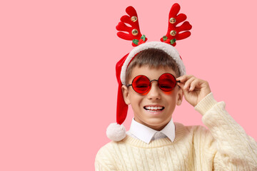 Happy little boy in Christmas reindeer horns with glasses on pink background