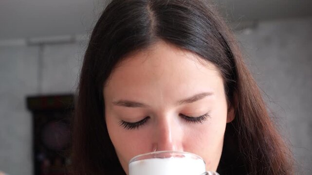 Close-up portrait captures a woman sipping espresso drink with milk foam mustache, delicately wiping her upper lip with a napkin in a casual, intimate moment.