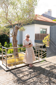 Elegant woman smiling and using smartphone outdoors in a sunny garden