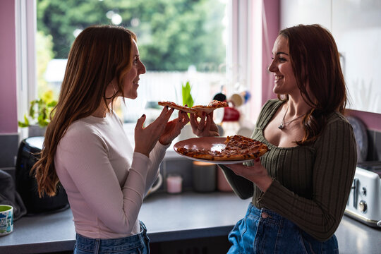 Friends smiling and sharing pizza in a modern kitchen at home - Powered by Adobe