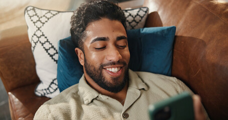 Home, smartphone and man in lounge, smile and social media with online comedy. Apartment, cellphone and person with happiness, email notification and connection with network, communication or texting
