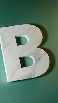 Vertical video: Showing white marble uppercase B staying flush left on green surface, copy space