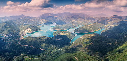 Aerial view showing Zaovine Lake reservoir, a dam, and surrounding mountains covered with forest