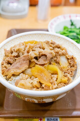 A Japanese beef bowl set meal from Sukiya, featuring simmered sliced beef over steamed rice, served with fresh vegetables and side dishes. The presentation highlights traditional Japanese fast food wi