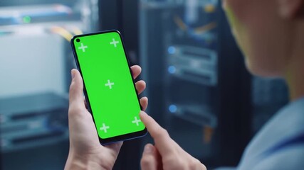 Closeup of a persons hands holding a smartphone with a green screen tapping and swiping in a data center or server room environment ideal for technology and IT concepts. - Powered by Adobe
