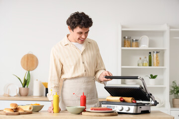 Young man grilling hot dogs in kitchen