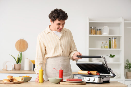 Young man grilling hot dogs in kitchen