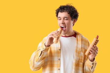 Young man eating tasty hot dogs on yellow background
