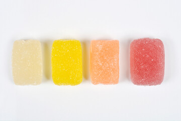 Four unwrapped, rectangular, sugar-dusted jelly candies are arranged in a horizontal row, showing colors from pale yellow to bright red on a white background