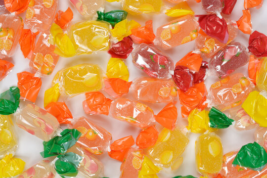 A full-frame, horizontal close-up of a dense scattering of various fruit-flavored jelly candies individually wrapped in brightly colored cellophane, covering a white background.