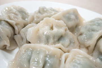 Fresh, delicious boiled garlic chives dumplings, jiaozi in white plate on wooden table background.