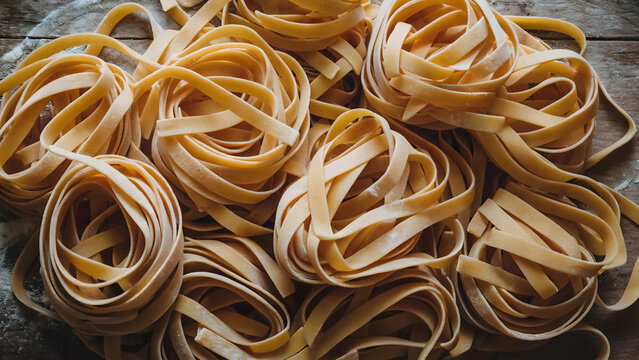 Artisanal fresh pasta nests on rustic wood surface ready for Italian family dinner or restaurant menu planning