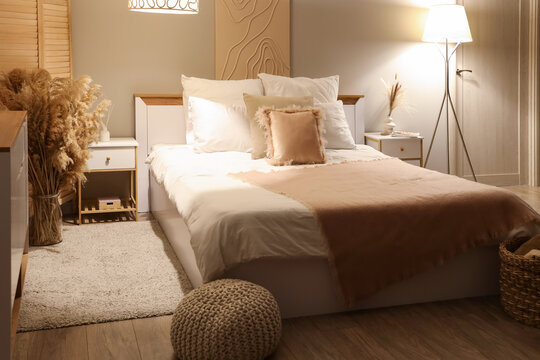 Interior of stylish room with bed, tables and glowing lamps at night - Powered by Adobe