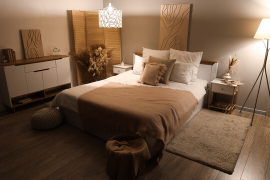 Interior of stylish room with bed, tables and glowing lamps at night