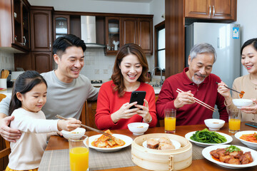Asian family group including young girl, young adult man, young adult woman, middle aged woman, senior man sitting at dining table eating traditional meal, smiling and interacting with smartphone