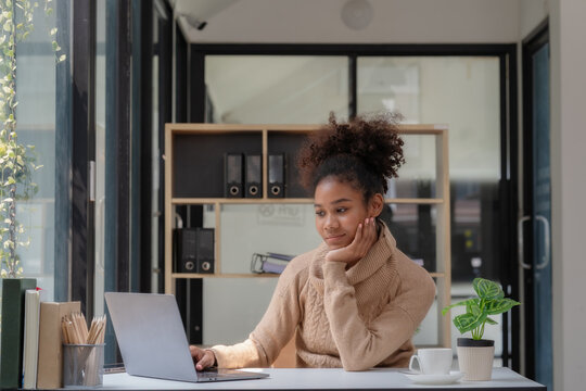 A happy professional businesswoman worker employee sitting at a desk working on a laptop in a corporate setting. A smiling female student using computer technology learning online, doing web research.