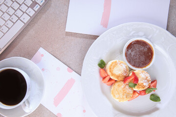 Cheesecakes with strawberries and jam. Healthy and nutritious breakfast. Computer keyboard is on the table. Concept of a business breakfast. Flat lay. Top view.