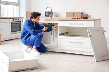 Male worker with drill assembling counter in kitchen