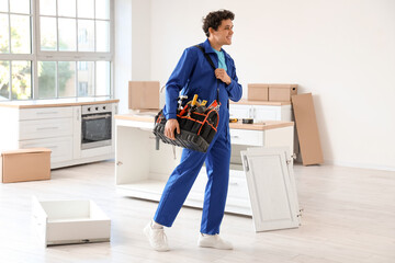 Male worker with tool bag assembling furniture in kitchen