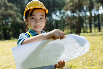 Happy child girl wearing yellow construction helmet or safety hard hat.