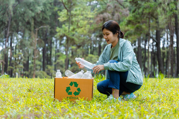 Young woman collects plastic bottles into recycling box in forest.