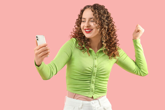 Happy young woman with mobile phone on pink background. Sports bet concept