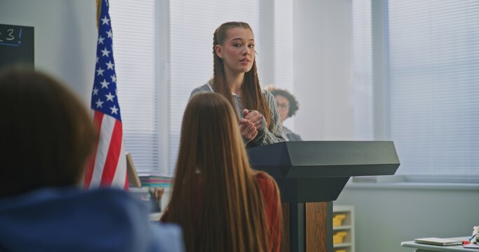 American Teenage Girl Delivers Expressive Speech in Front of Classmates, Gesturing Confidently With US Flag. Concept Civic Education, Confident Communication, Active Student Participation. Dolly Shot.