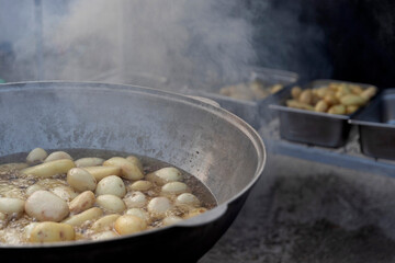 Small white potatoes boiling in a large cauldron or pot over heat with visible steam, with more cooked potatoes blurred in the background.