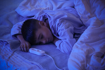 Little boy sleeping under blanket on electric heating pad in bedroom at night