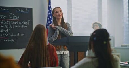 American Teenage Girl Delivers Expressive Speech in Front of Classmates, Gesturing Confidently With US Flag. Concept Civic Education, Confident Communication, Active Student Participation. Dolly Shot.