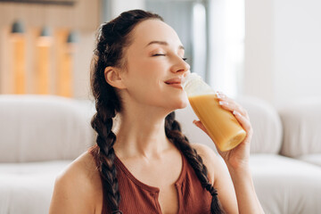 Cheerful beautiful middle aged woman drinking orange juice, holding bottle enjoying with closed eyes