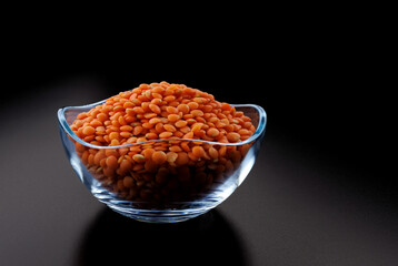Red lentils in a transparent glass cup on a black background. Side view. Beautiful highlights on the black background.
