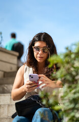 Young woman sitting looking at her cell phone in the city