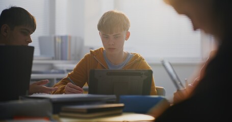 Close Up of Focused Young Man Working on Tablet in Classroom, Surrounded by Classmates. Boys Discussing Educational Project. Concept Modern Learning, Collaborative Learning, and Digital Technologies.