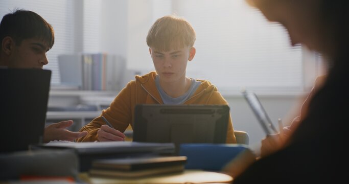 Close Up of Focused Young Man Working on Tablet in Classroom, Surrounded by Classmates. Boys Discussing Educational Project. Concept Modern Learning, Collaborative Learning, and Digital Technologies.