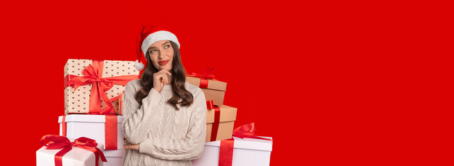 A cheerful young woman wearing a holiday headband stands next to a collection of beautifully wrapped gifts. The bright red background adds a joyful touch to the festive mood.