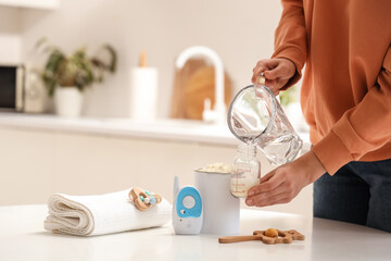 Woman preparing baby milk formula at table in kitchen