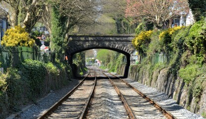 Railway tracks pass under a stone arch bridge surrounded by lush greenery.