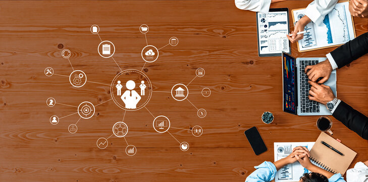 Aerial view of a professional business meeting showcasing collaboration and data analysis with digital icons, documents, and two engaged individuals at a wooden desk. Trope - Powered by Adobe