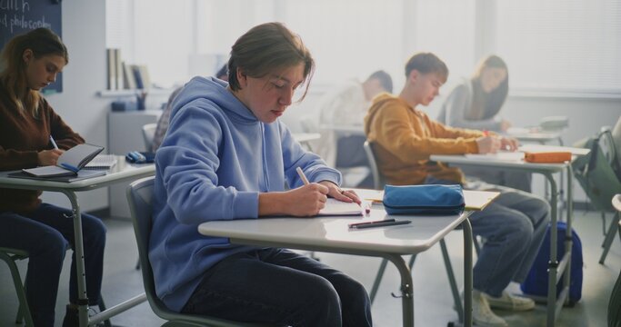 Young Boy Concentrates on Writing Task in Class. Other Students Working at Desks. Concept Student Focus, Academic Concentration, Process of Independent Work in Modern School Setting. Static Shot.