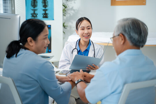 Smiling Asian female doctor in a white coat providing a positive health consultation to an elderly couple in her modern clinic office, with the senior man and woman holding hands. Concept of geriatric