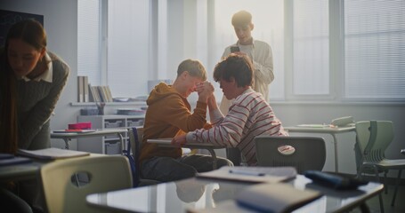 Students Playfully Arm Wrestle at Desk During Break, Surrounded by Laughing Friends. Concept of Youthful Energy, Friendly Competition, and Positive Peer Interaction in Modern School Environment.