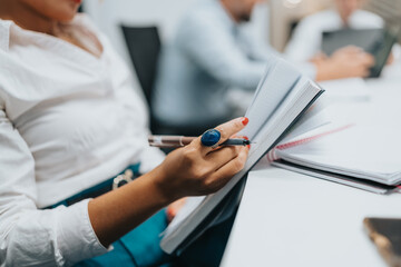 Business scene showing a woman writing in a notebook while reviewing documents in a meeting.