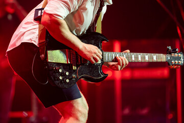 Male musician performing on stage and playing electric guitar during a live concert show with stage lights and sound equipment