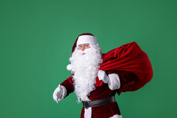 Santa Claus with red bag of Christmas gifts on green background