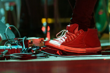 Closeup of a man’s feet pressing knobs on electric guitar pedals during a live performance, controlling sound effects and tone adjustments on stage