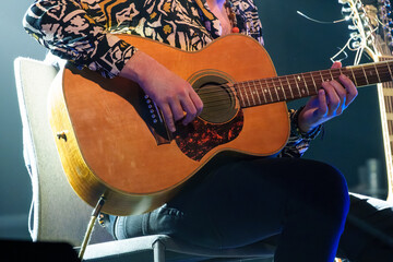 Male musician performing on stage and playing electric guitar during a live concert show with stage lights and sound equipment